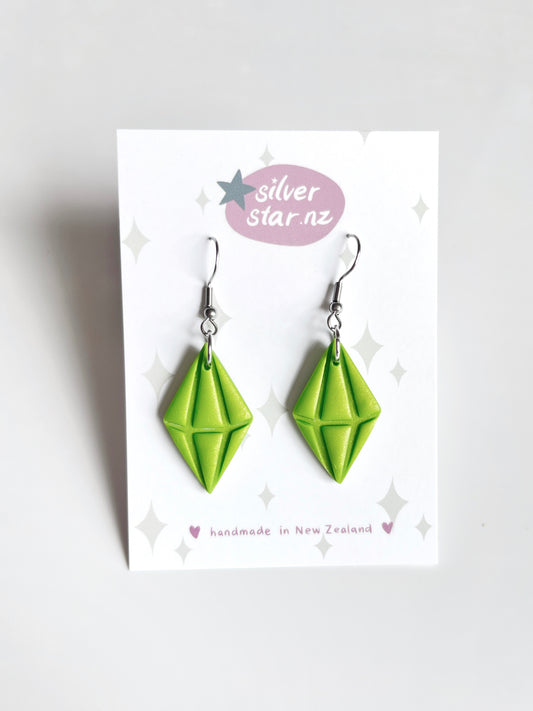 Displayed on a white card labeled silverstar.nz, the Sims Plumbob Polymer Clay Earrings feature a unique geometric design in vibrant green, meticulously crafted from handmade polymer clay in New Zealand. Stainless steel hooks enhance their modern elegance, ensuring style and durability.