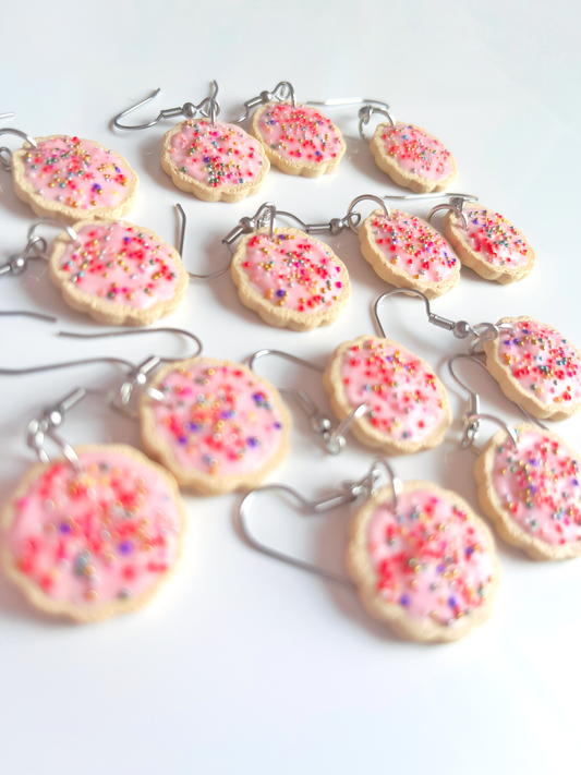 Hundreds and Thousands Biscuit Earrings by silverstar.nz are handmade polymer clay earrings with pink icing and colorful sprinkles, presented on a white surface. Featuring stainless steel hooks, the playful cookie-themed design is arranged randomly for a whimsical appearance.