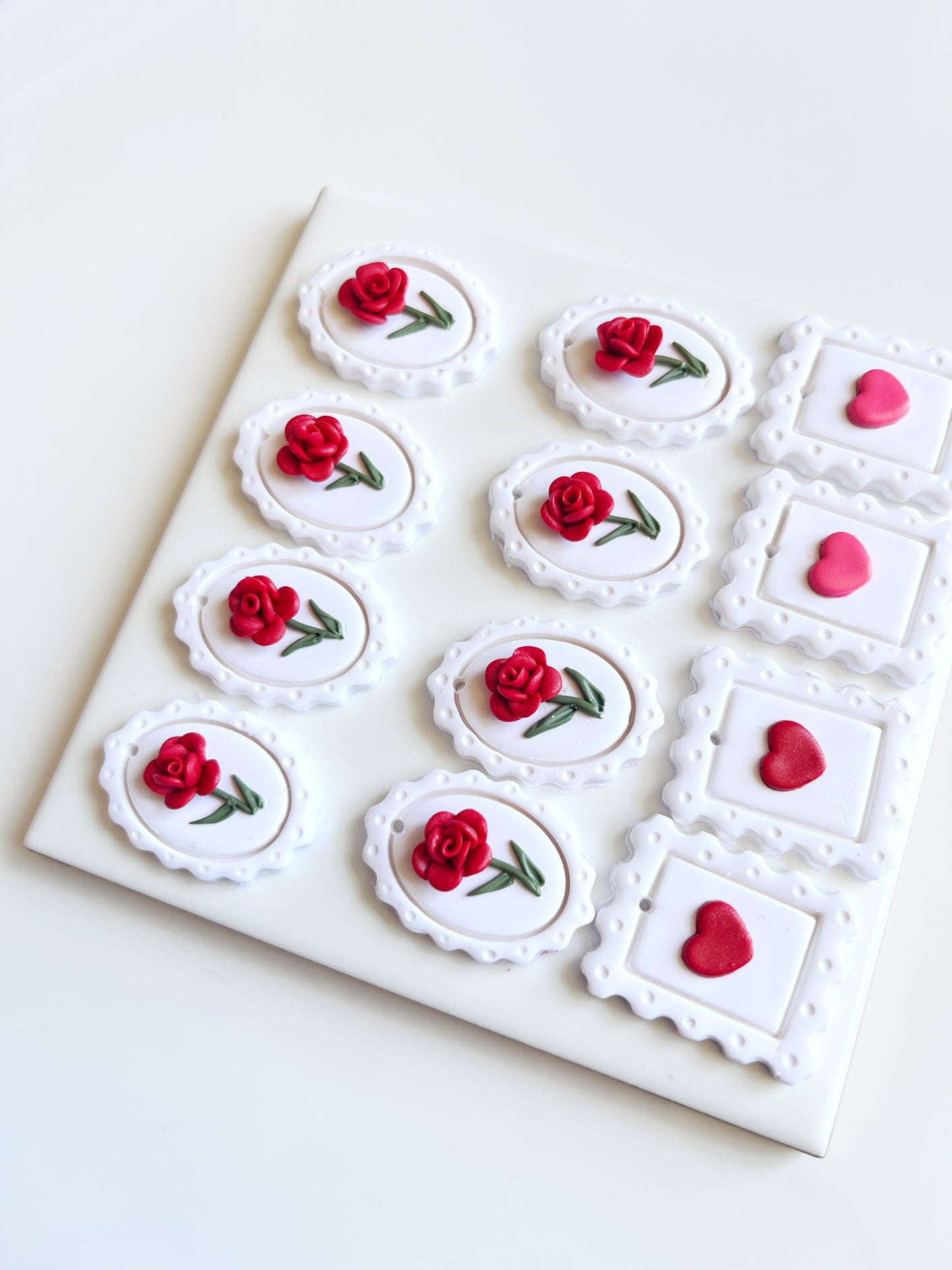 A square board features six oval cookies with red roses and four square cookies with pink hearts, echoing the distinctive design of silverstar.nzs Framed Rose Polymer Clay Earrings. Each cookies decorative edges reflect the craftsmanship of these handmade earrings, arranged neatly in a grid.