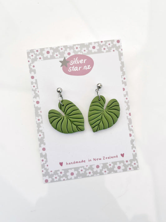 The Heart Leaf Polymer Clay Earrings by silverstar.nz are uniquely designed in green, shaped like leaves, and displayed on a decorative card with pink flowers and heart borders. The card notes handmade in New Zealand at the bottom.