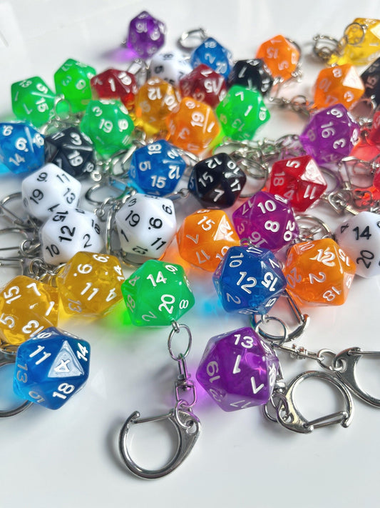 A selection of silverstar.nz D20 Dice Keyrings is spread across a white surface, featuring shapes like 20-sided dice. These vibrant accessories are perfect for any Dungeons and Dragons enthusiast, available in bright hues such as green, purple, orange, and blue with numbers marked on each side.