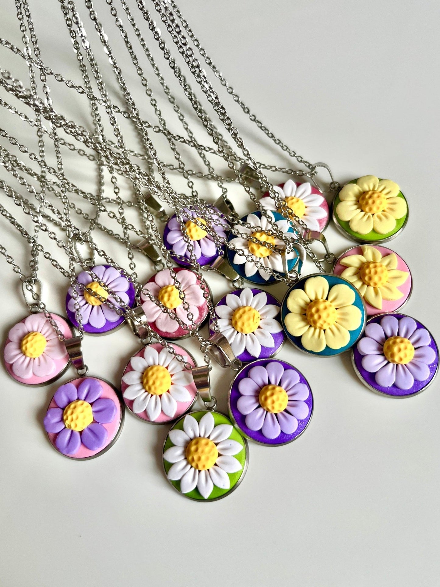 A selection of vibrant Daisy Polymer Clay Necklaces from silverstar.nz is beautifully arranged on a white surface. Each handmade pendant showcases a daisy-like design in an array of colors—purple, yellow, and pink—set against backgrounds of green, pink, and blue. These necklaces are perfect examples of exquisite New Zealand jewelry craftsmanship.