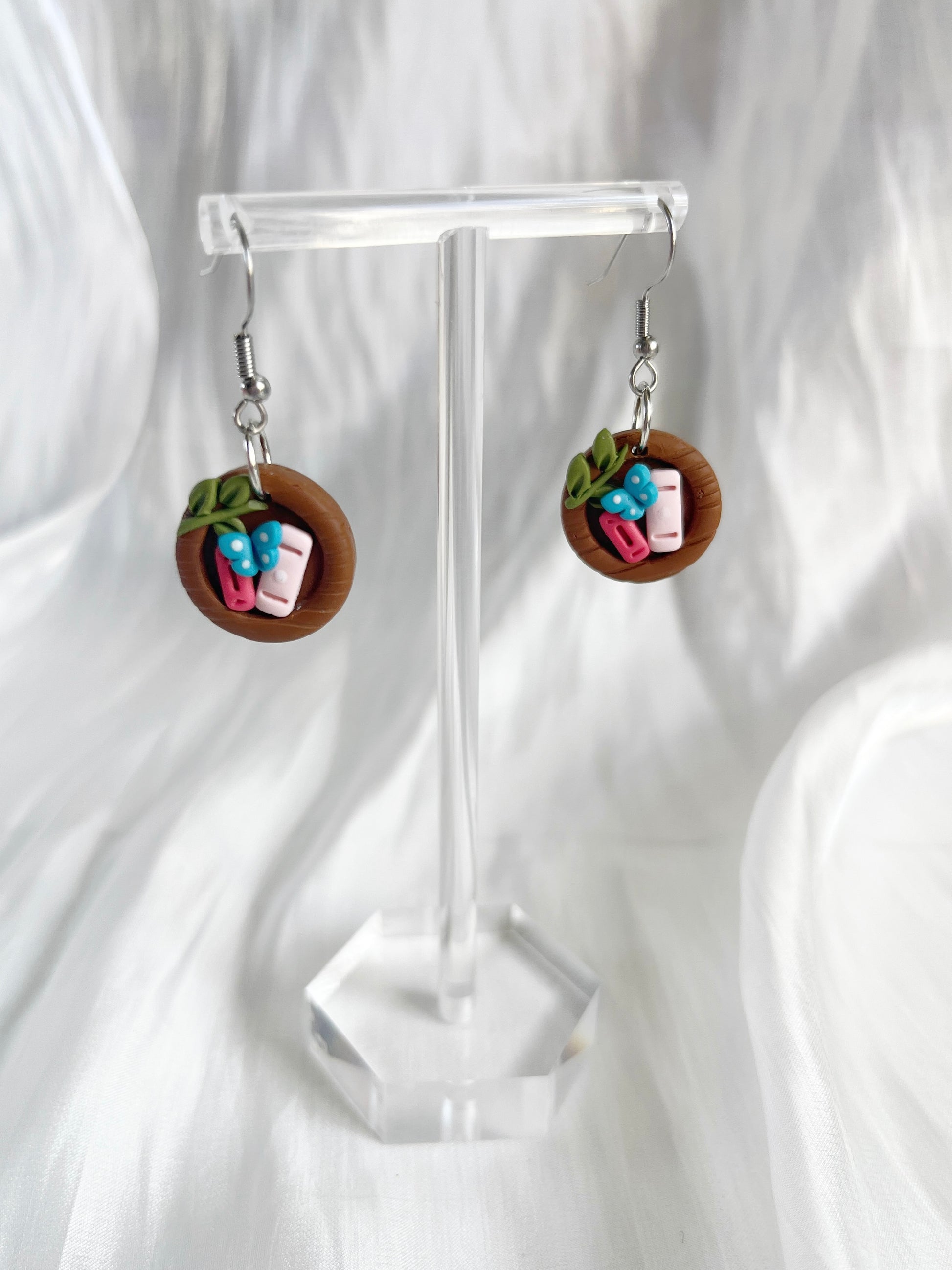 The Mini Round Bookshelf Polymer Clay Earrings by silverstar.nz feature a unique wooden plate design with miniature sushi rolls, including pink fish and green leaves, displayed on a transparent stand against a white background.