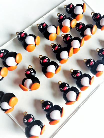 A group of small, handmade penguin figurines featuring black bodies, white bellies, and orange feet and beaks is displayed on a white surface. Each wide-eyed penguin is crafted with precision similar to Pingu Polymer Clay Earrings, adding charm and whimsy to any space.