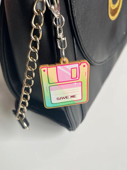 Close-up of a black bag with a chain strap, showcasing the Floppy Disk Acrylic Keyring, artistically designed in vibrant colors and labeled with "SAVE ME" at the center.