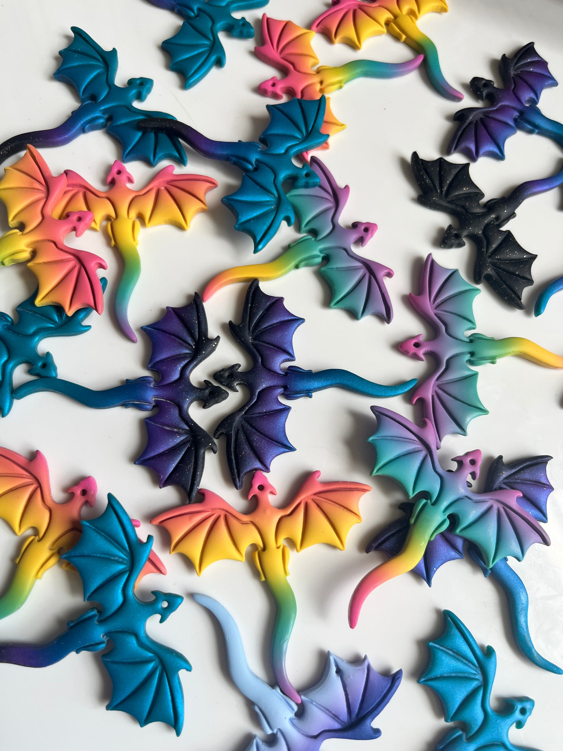 The Blue Dragon Polymer Clay Earrings by silverstar.nz are seen scattered across a white background. Their design is reminiscent of colorful, intricately crafted dragon cookies, featuring funky wing patterns and vivid shades of blue, pink, yellow, purple, and black.