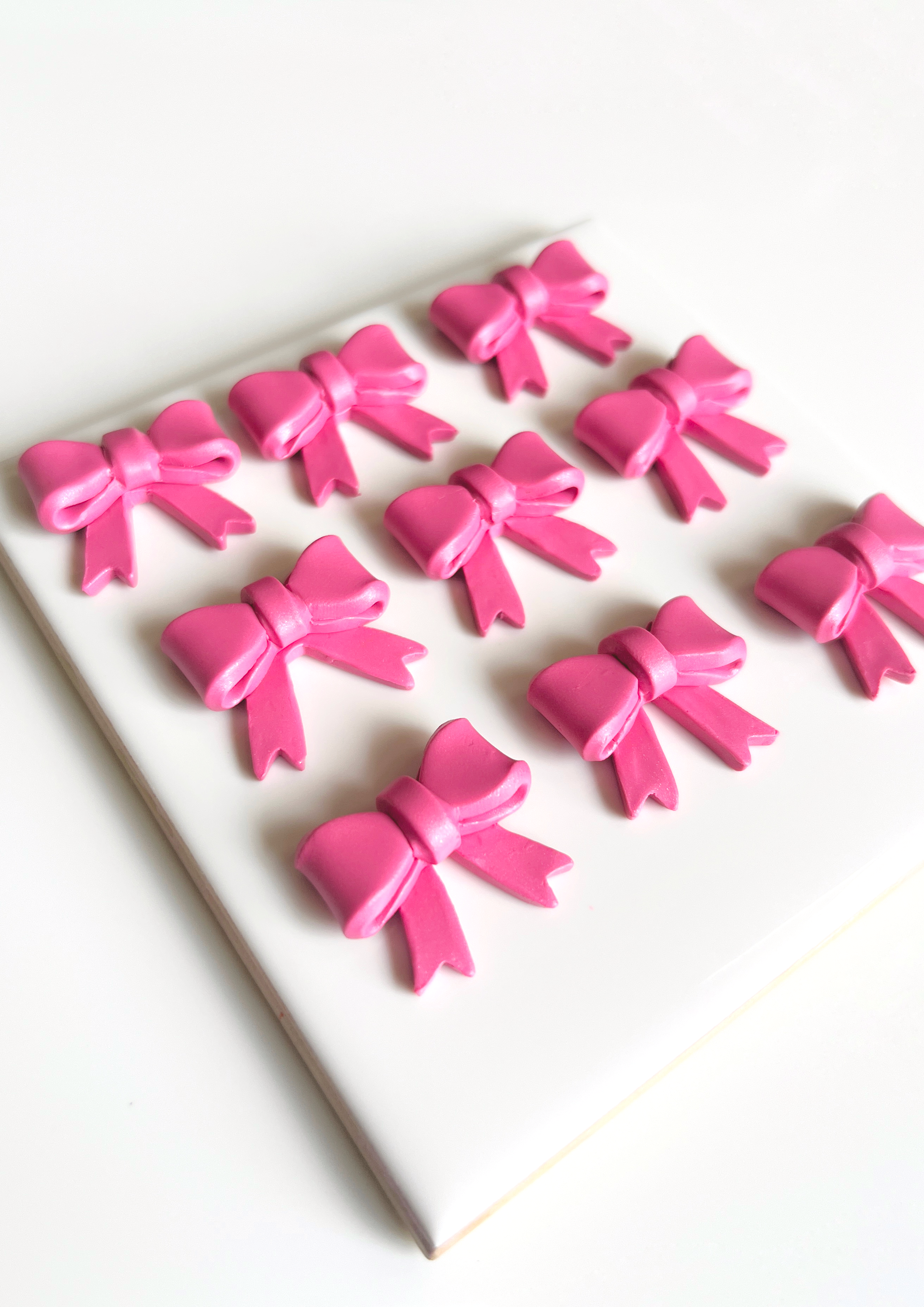 The image features Bow Coquette Polymer Clay Earrings from silverstar.nz, beautifully arranged on a white ceramic tile with nine pink ribbon bows aligned in a 3x3 grid, creating a charming symmetrical pattern against the pristine background.
