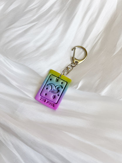 The Tarot Card Polymer Clay Keyring by silverstar.nz is a rectangular accessory with a funky design, featuring a colorful gradient from yellow to purple. It includes a jester hat and THE FOOL text on silky white fabric, ideal for fans of New Zealand handcrafted pieces.