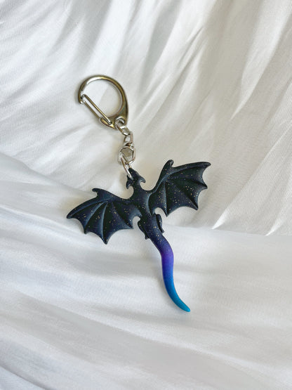 The Midnight Blue Dragon Polymer Clay Keyring by silverstar.nz features a dragon-shaped accessory with black wings and a blue-to-purple gradient tail on a textured white fabric background, making it the perfect imaginative gift.