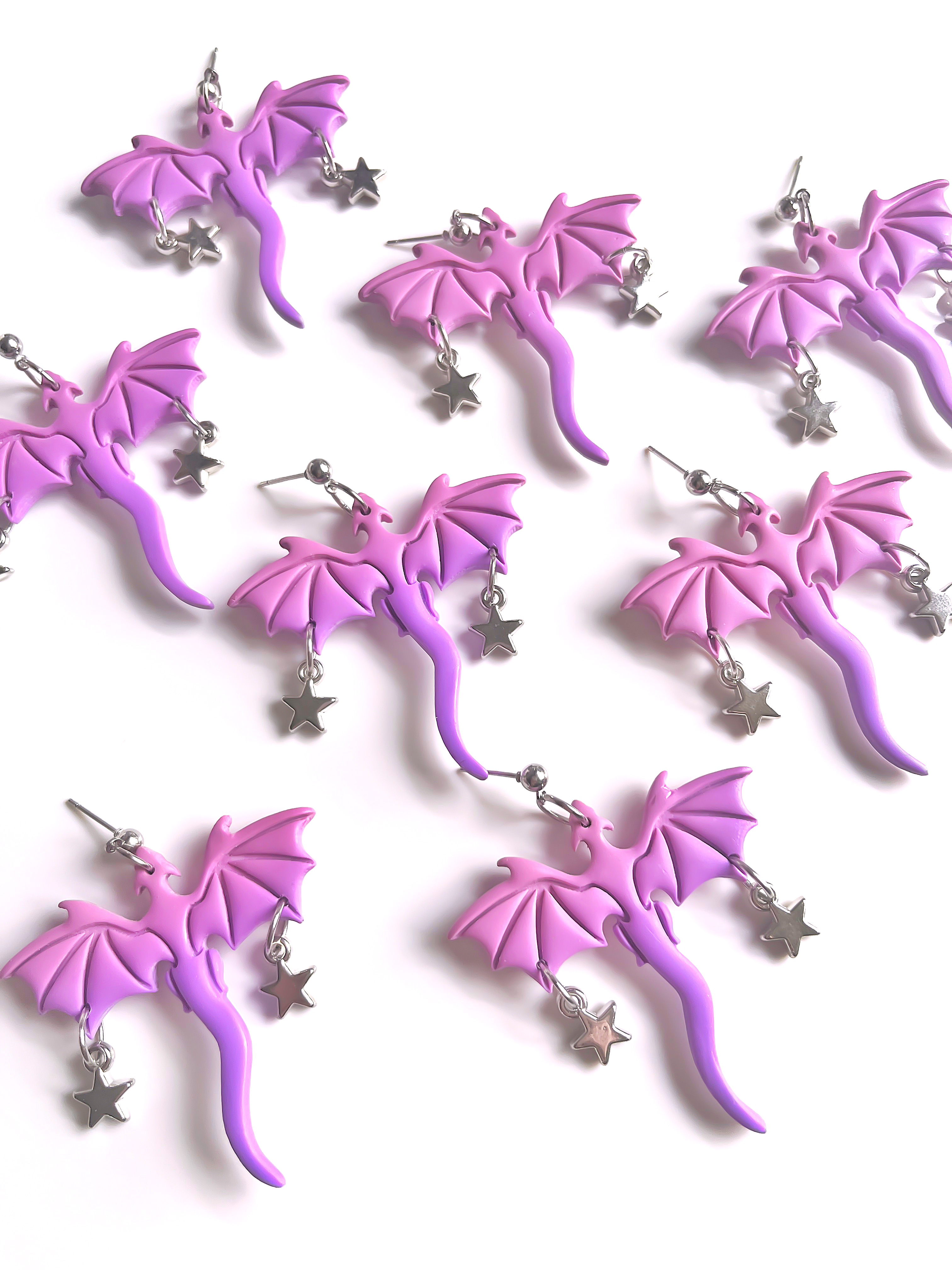 Purple Dragon Polymer Clay Earrings by silverstar.nz are artfully crafted in a dragon shape with star charms. Displayed on a white background, these unique earrings feature detailed wings and tails, showcasing the glossy finish and craftsmanship of handmade jewelry.