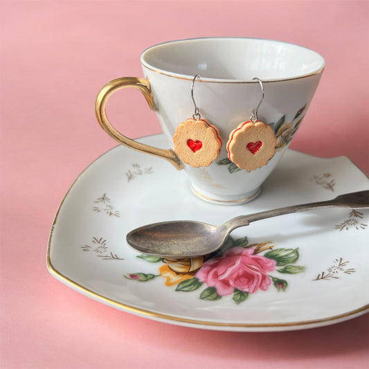 Shrewsbury Polymer Clay Earrings displayed on a tea cup. There is also a pretty saucer and tea spoon with a pink background.